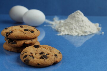 kitchen cooking process homemade chocolate cookies with chocolate drops in the background flour and chicken eggs lie on a blue bright rich mirror background side view with a reflection of copy space
