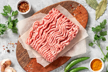 Raw uncooked minced pork on a wooden cutting board top view. Grey concrete background.