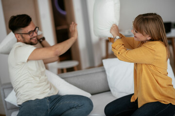 Obraz premium Husband and wife fighting pillows on the bed. Young couple having fun at home.