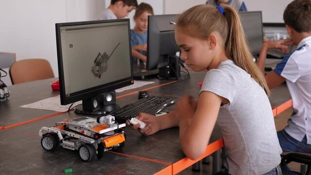 Group of kids building robot constructor from the plastics details programmed on the computer, at robotics school lesson.