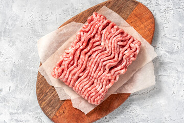 Raw uncooked minced pork on a wooden cutting board top view. Grey concrete background.