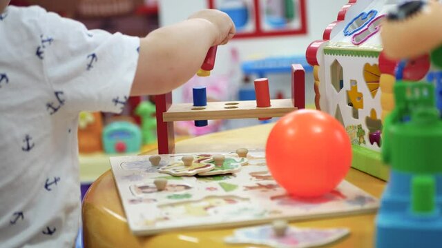 Children's hands play a colorful punching sorter in a large entertaining children's room. Environmentally friendly wooden kids toys. Study of shapes, colors, structure.