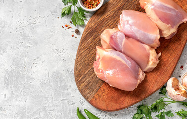 Raw uncooked skinless chicken thighs on a wooden cutting board top view. Raw poultry fillet on a grey concrete background. Copy space for text