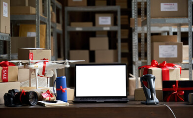 Table with electronic devices and laptop computer mock up blank white on table, warehouse storage background. Ecommerce gadgets store website discount gifts. Black friday and cyber monday concept.