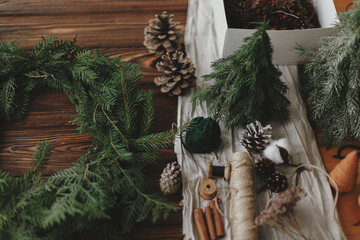Making rustic christmas wreath on wooden table. Christmas wreath, green branches, pine cones, twine