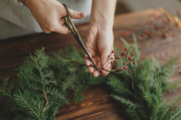 Making rustic christmas wreath, seasonal winter workshop. Florist  holding scissors and berries