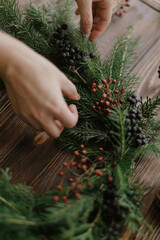 Making rustic christmas wreath, seasonal winter workshop. Florist holding berries on wooden table