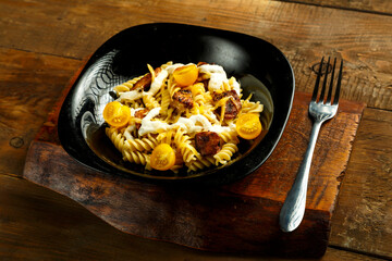 Pasta with chicken and cheese in a black plate on a wooden stand with a fork.