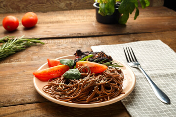 A plate of soba with chicken, tomatoes and spinach on a linen napkin next to a fork on the table with vegetables.
