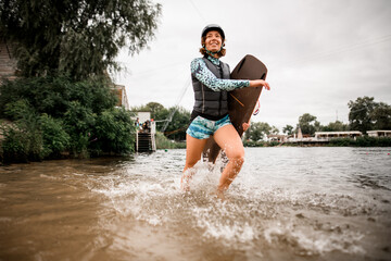 woman with helmet and wakeboarding board running on water along the river bank