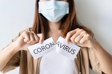 Portrait of young Asian woman wearing medical mask tears the paper with the word Coronavirus. Pandemic of COVID-19 is over. Stop spread and eliminate Coronavirus concept. Isolated on white background