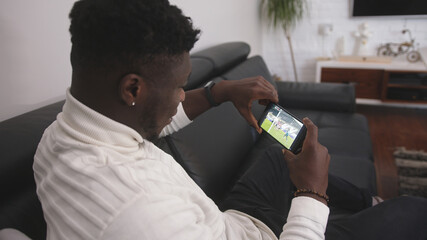 Young excited black man watching football game on the smartphone. High quality photo