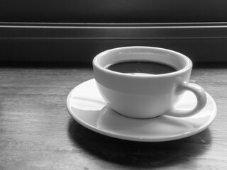 A black and white picture of a white coffee cup placed on a wooden table.