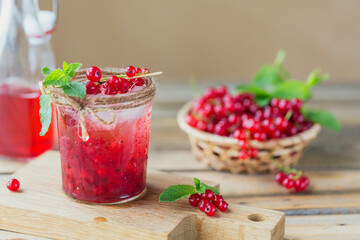 Glass of red currant cocktail or mocktail, refreshing summer drink with crushed ice and sparkling water on a wooden background.