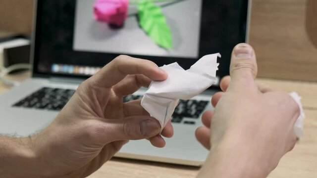 Male hands making origami figure from white paper. Stock footage. Man fails to make a flower from paper like on a picture on a computer screen,