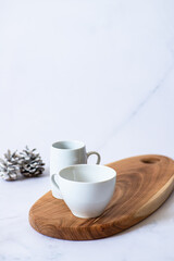 Two white cups on a wooden board on a light marble background with festive winter decorations. Winter mood. Close up. Selective focus 