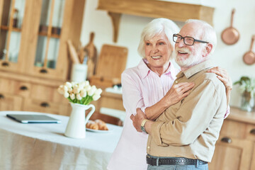 Smiling elder couple embracing while standing at home