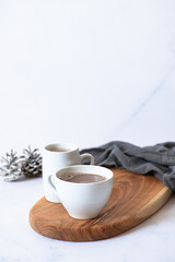 Two white cups with hot chocolate or cocoa drink on a wooden board on a light marble background with festive winter decorations. Winter mood. Frontal view. Copy space. Selective focus