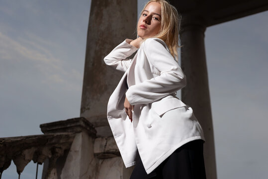 portrait of a blonde model, fashion girl in a white jacket, posing, against the background of vintage columns. beauty and fashion of young teenage girls, generation Y