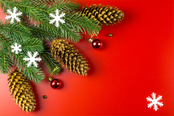 Snowflakes, fir branches and holiday decorations on a red background with space for text.