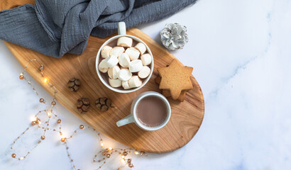 Winter breakfast with cookies, hot chocolate, cocoa drink with marshmallows, served on a wooden board and a marble table with festive Christmas decorations