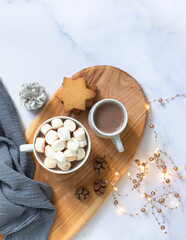 Winter breakfast with cookies, hot chocolate, cocoa drink with marshmallows, served on a wooden board and a marble table with festive Christmas decorations