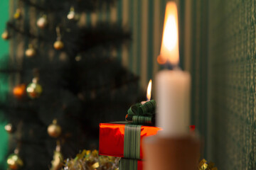 A candle is burning in the foreground out of focus, gifts and a Christmas tree in focus in the background