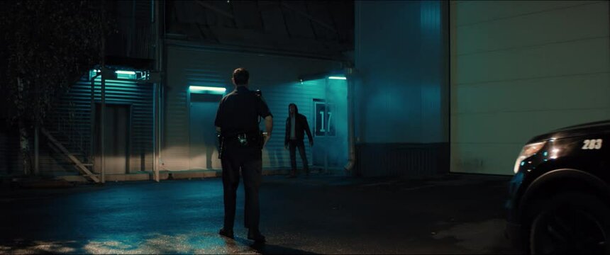 WIDE Police car turns on flashing lights while approaching two multi-ethnic males suspects near industrial buildings at night. Shot on RED cinema camera with 2x Anamorphic lens