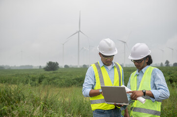 Two engineers working and holding the report at wind turbine farm Power Generator Station on mountain,Thailand people