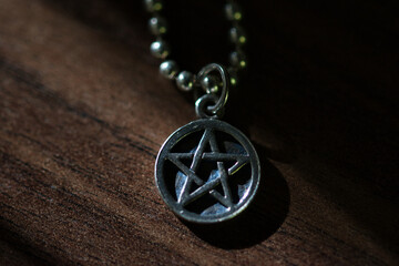 Fototapeta na wymiar Silver Pentagram charm old necklace on a dark brown wooden surface, light and shadows contrasts, magic, mystic and protection concept web background 