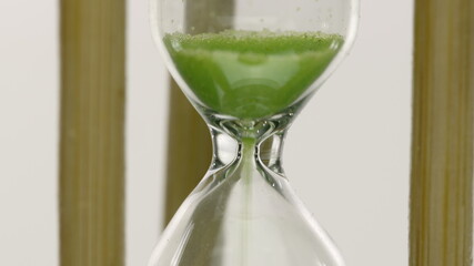 Close up hourglass countdown isolated on white background. Light green sand falling move through sandglass. Passing time, deadline, loading, timer, earth care save life concept, time is over. Zoom in