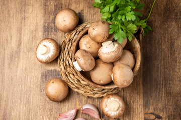 Aerial view of portobello mushrooms in wooden bowl with parsley and garlic, on wooden table, horizontal