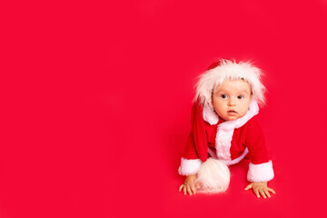 a surprised little child six months old in a Santa costume sits on a red isolated photophone, a place for text, a new year and holiday concept