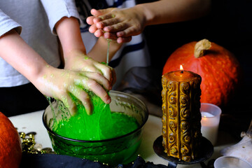 children play with a green witchcraft potion, table is covered with a black cloth, pumpkins lie,...