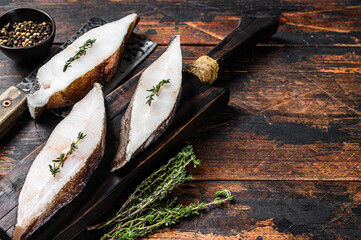 Raw fresh halibut fish steak on a wooden cutiing board. Black background. Top view. Copy space
