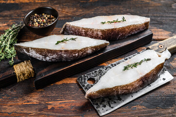 Raw fresh halibut fish steak on a wooden cutiing board. Black background. Top view - obrazy, fototapety, plakaty