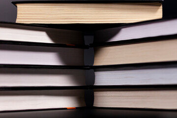 Neat straight stacks of books on a dark background. Closeup. Side view.