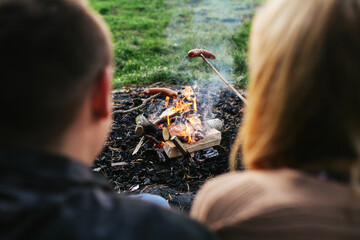 Sausage roasting on fire. Couple cooking together. Bonfire cooking in forest. Campfire picnic...