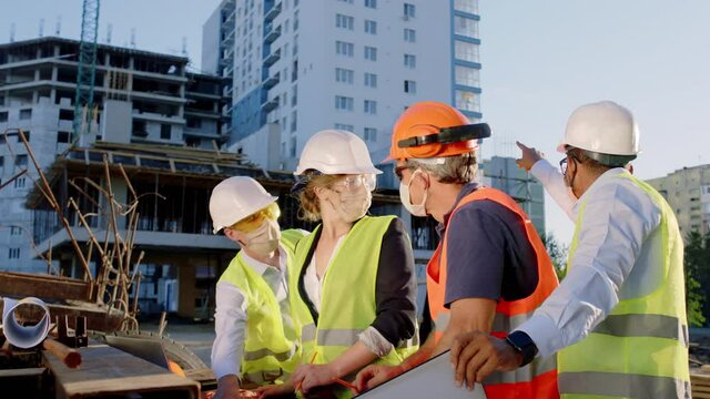 At construction site group of diverse specialists multiracial analyzing the plan of construction site they wearing protective mask and safety equipment in the pandemic of Coronavirus