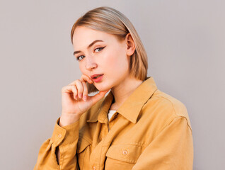 Close-up portrait of blond woman with hand near face looking at camera on gray background