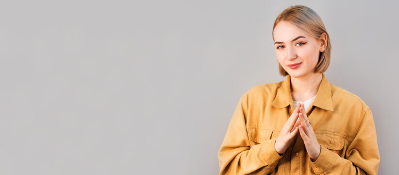 I have great evil plan. Good-looking confident and tricky woman in beige blouse, holding fingers together and smirking at camera, having some bad intention in mind, planning to commit crime