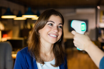 A faceless office worker checks a woman's fever with an infrared thermometer in the office