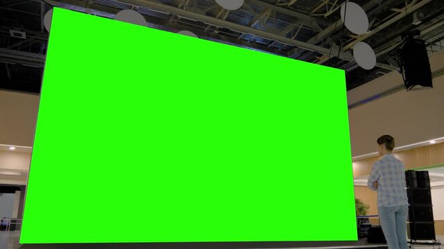 Woman looking at large wall blank interactive green display in bright room of modern technology exhibition or museum. Mock up, green screen, futuristic, template, education, chroma key concept