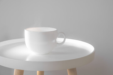 Mug with hot drink on a white coffee table indoors. Scandinavian interior style, minimalism in house, tranquil living concept