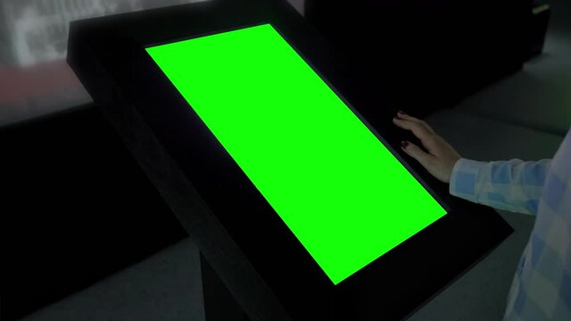 Green screen, futuristic, mockup, science, copyspace, template, chroma key, technology concept. Woman looking at blank green display of interactive kiosk in dark room of exhibition or museum