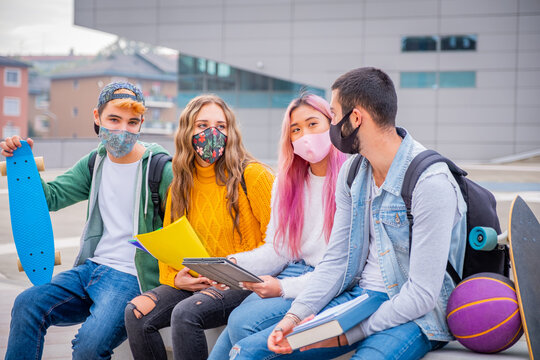 Multiethnic Students Sitting With Mask  On The Bench Together In A University - Group Of Young Teenagers Studying On The Bench With Protective Mask In Pandemic Covid 19 Period