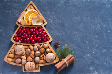 Nuts, cranberries and dried fruit in Christmas tree-shaped bowl on dark background