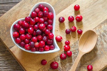 Ripe cranberry in heart-shaped bowl on wooden board