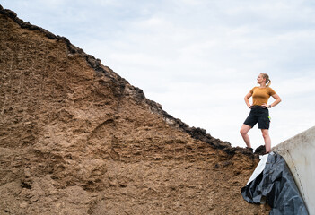Naklejka premium Junge Landwirtin steht an einem großen Maissilagehaufen, landwirtschaftliches Symbolfoto.