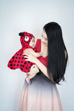 An asian baby girl wearing a ladybug bodysuit wih a young mother on white background, focusing on baby;
